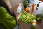 Woman holding a Bio-Design bottle with cutting board of fresh vegetables in front of her